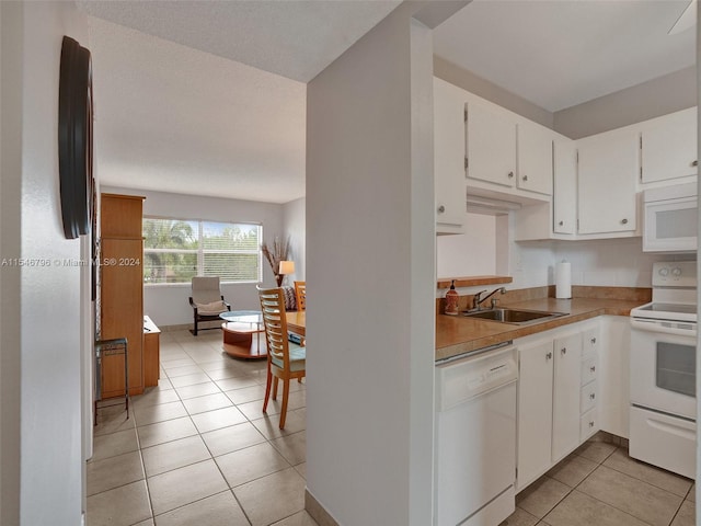 kitchen featuring white appliances, light tile flooring, white cabinetry, and sink