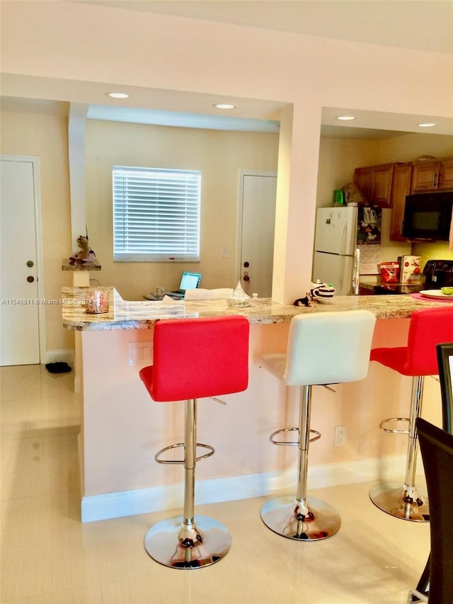 kitchen with light tile floors, a kitchen bar, light stone countertops, and white refrigerator