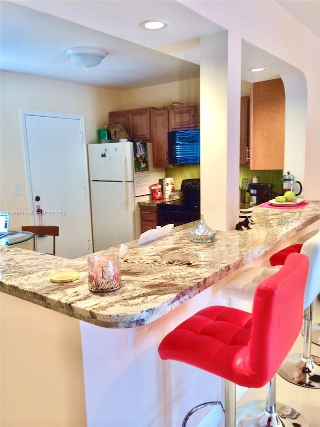 kitchen featuring white fridge, light stone countertops, kitchen peninsula, a breakfast bar, and range