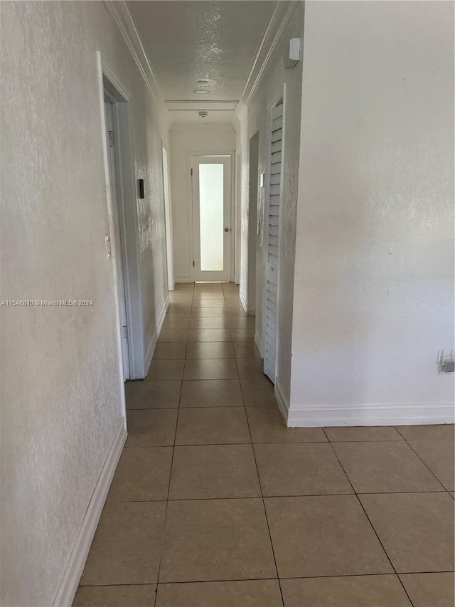 corridor with tile patterned floors, crown molding, and a textured ceiling