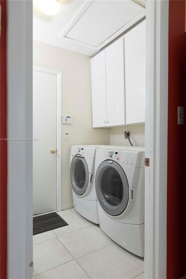 laundry area with washing machine and clothes dryer, cabinets, and light tile flooring