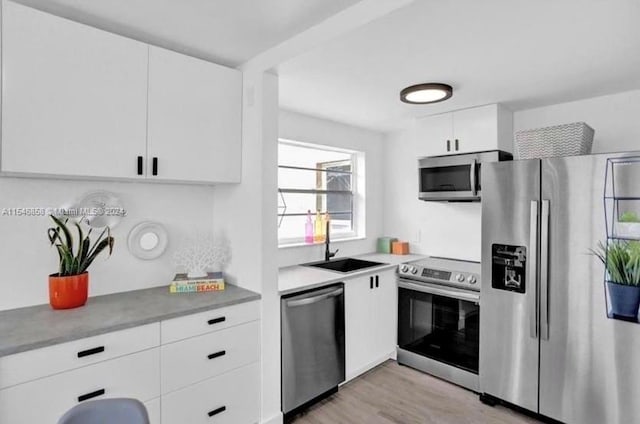 kitchen with stainless steel appliances, sink, white cabinetry, and light wood-type flooring