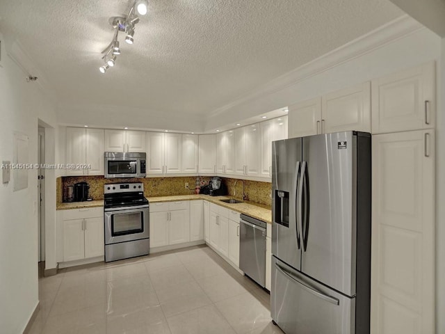 kitchen with track lighting, stainless steel appliances, white cabinets, a textured ceiling, and ornamental molding