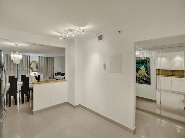 tiled spare room with an inviting chandelier, a textured ceiling, rail lighting, and ornamental molding