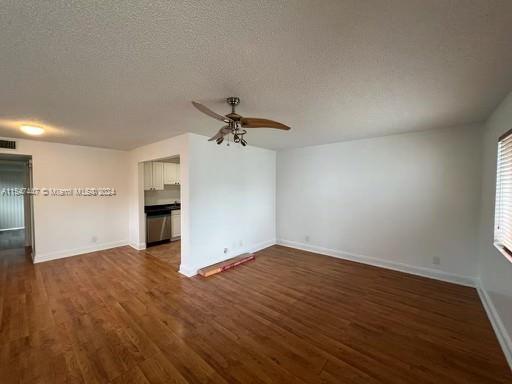 unfurnished living room with a textured ceiling, ceiling fan, and dark wood-type flooring