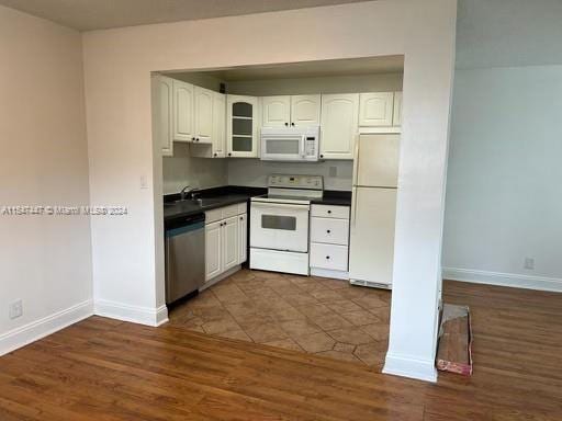 kitchen with white appliances, dark tile floors, white cabinets, and sink