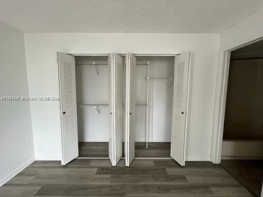 unfurnished bedroom with a textured ceiling, dark wood-type flooring, and two closets