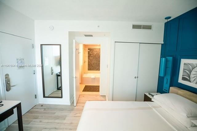 bedroom with ensuite bathroom, light hardwood / wood-style floors, and a closet