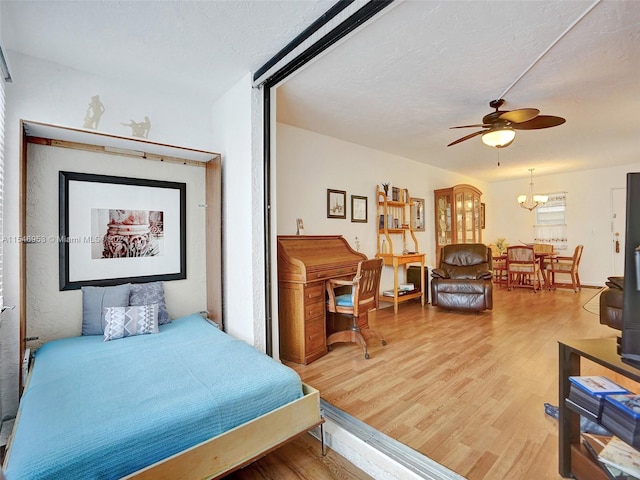 bedroom with ceiling fan with notable chandelier and light hardwood / wood-style flooring