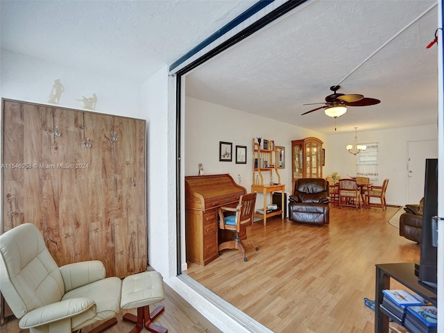 living area featuring a textured ceiling, ceiling fan with notable chandelier, and light wood-type flooring