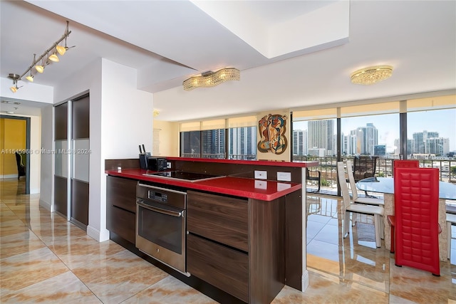 kitchen featuring light tile floors, oven, rail lighting, expansive windows, and black electric stovetop