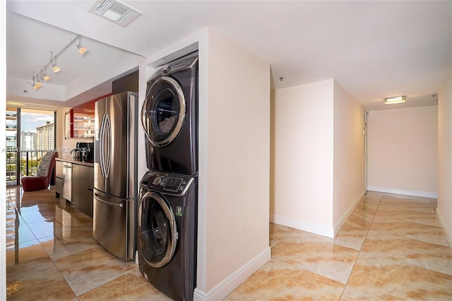 washroom with light tile floors, stacked washer and dryer, and rail lighting