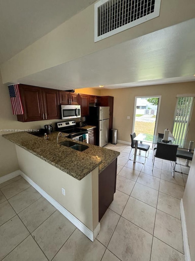 kitchen featuring kitchen peninsula, dark stone countertops, light tile floors, sink, and appliances with stainless steel finishes