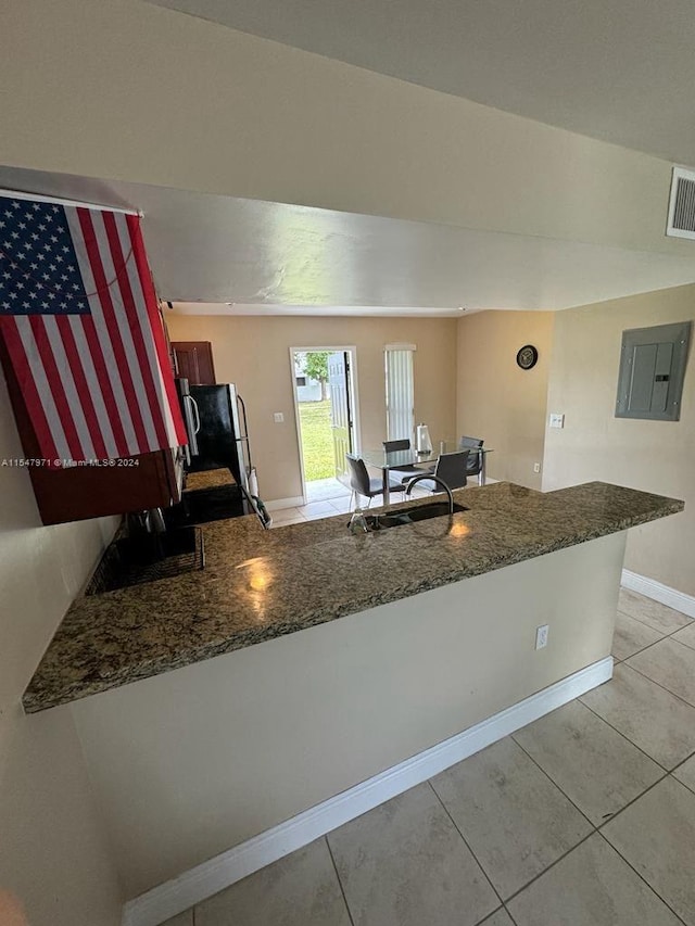 kitchen featuring refrigerator, dark stone counters, and light tile floors