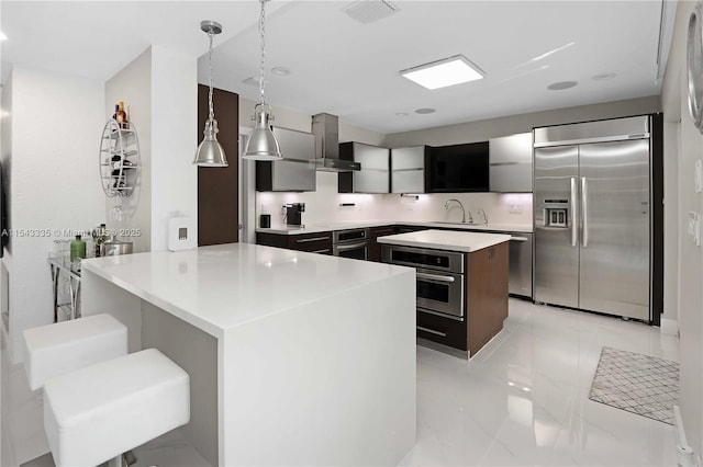 kitchen featuring decorative light fixtures, a kitchen island, sink, appliances with stainless steel finishes, and wall chimney exhaust hood