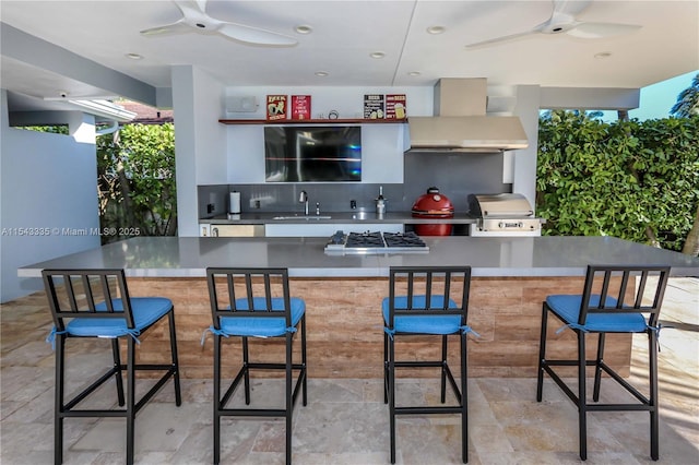 kitchen featuring decorative backsplash, a kitchen breakfast bar, stainless steel gas cooktop, wall chimney range hood, and sink