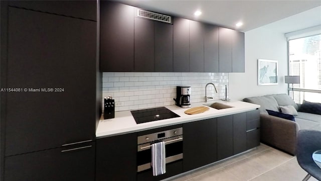 kitchen with light tile patterned flooring, tasteful backsplash, stainless steel oven, black electric cooktop, and sink