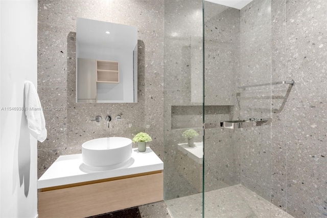 bathroom with a tile shower, vanity, and tile walls