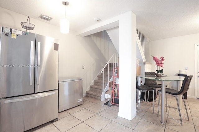 kitchen with stainless steel fridge, refrigerator, light tile patterned flooring, and a textured ceiling