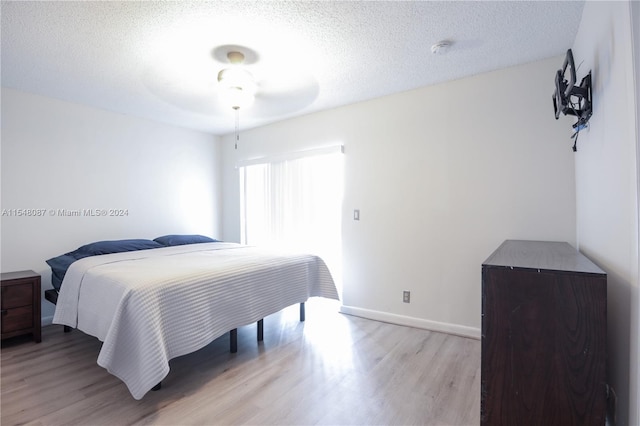 bedroom with a textured ceiling, light wood-type flooring, and ceiling fan