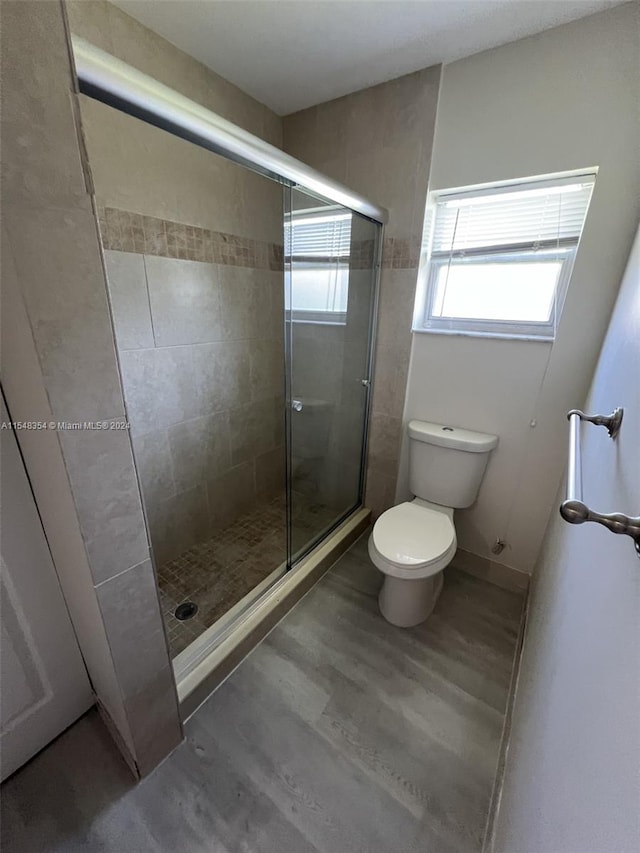 bathroom featuring hardwood / wood-style flooring, toilet, and a shower with shower door