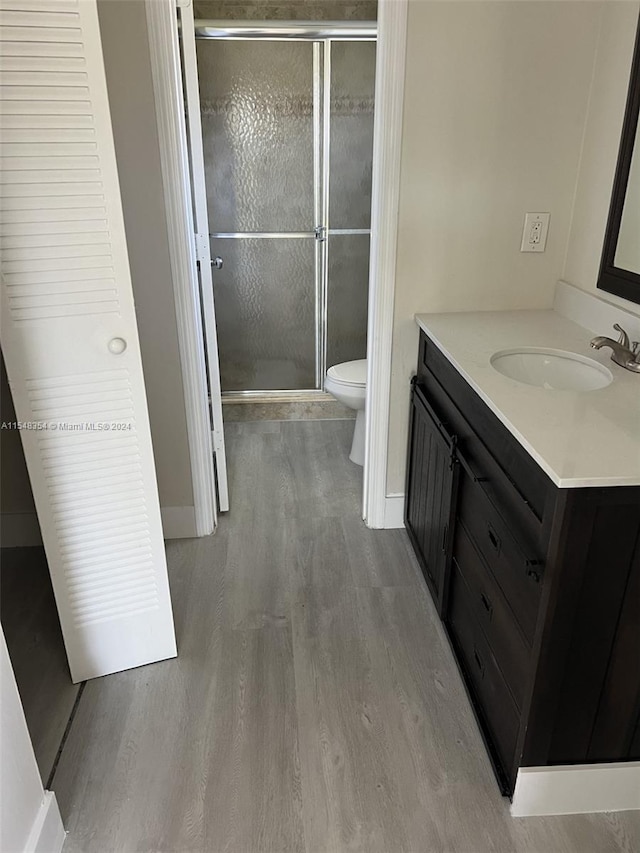 bathroom with wood-type flooring, a shower with door, vanity, and toilet