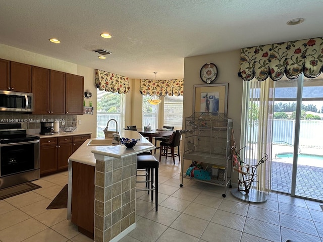 kitchen with tasteful backsplash, pendant lighting, an island with sink, sink, and appliances with stainless steel finishes