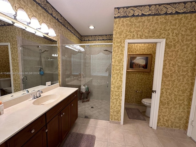 bathroom with a shower with door, vanity, toilet, and tile patterned floors