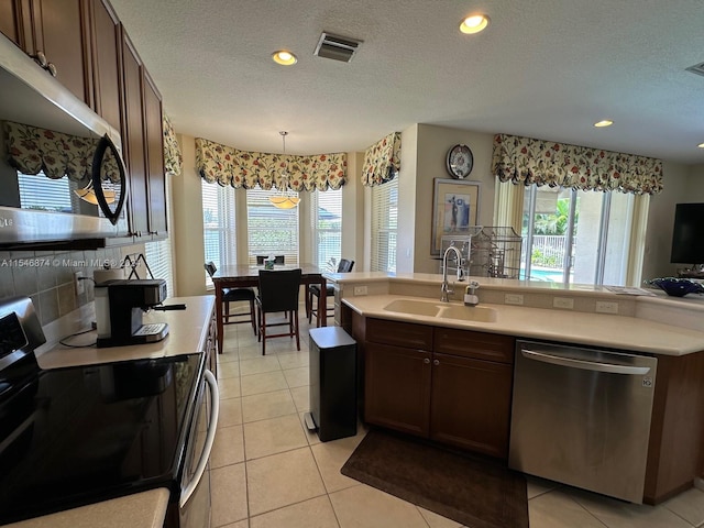 kitchen featuring appliances with stainless steel finishes, sink, pendant lighting, light tile patterned floors, and a textured ceiling