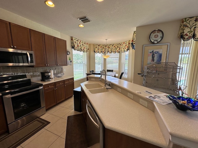 kitchen featuring light tile patterned flooring, tasteful backsplash, appliances with stainless steel finishes, pendant lighting, and sink