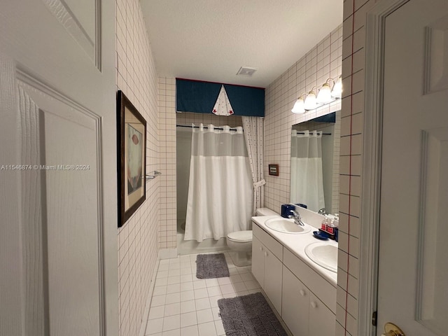 bathroom with tile walls, tile patterned flooring, a textured ceiling, toilet, and double sink vanity