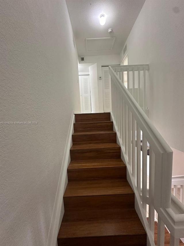 stairs with a textured ceiling and dark hardwood / wood-style flooring