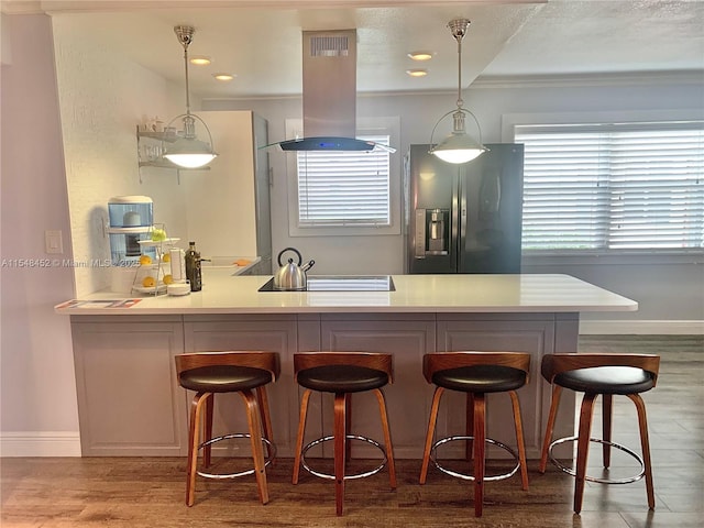 kitchen featuring fridge with ice dispenser, hanging light fixtures, kitchen peninsula, a kitchen bar, and island range hood