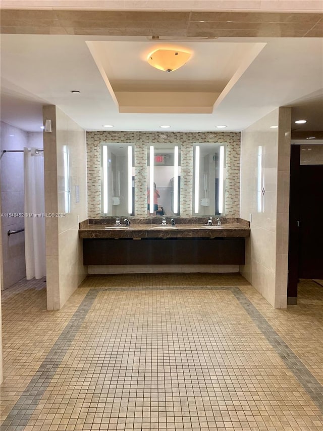 bathroom with tile patterned floors, vanity, a raised ceiling, and tile walls