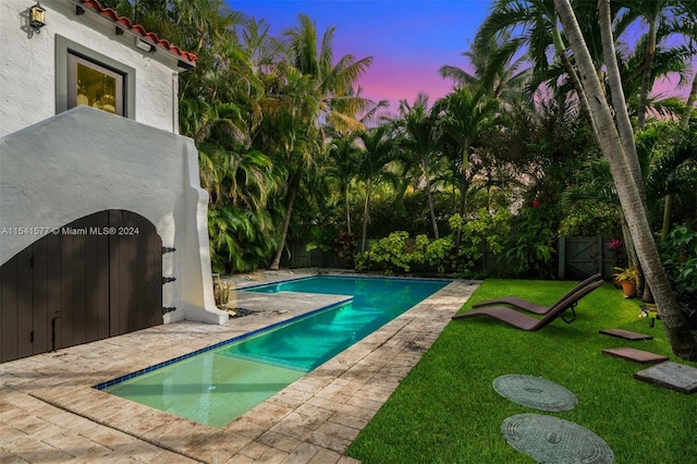 pool at dusk with a patio area and a yard