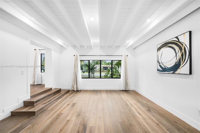 spare room featuring light wood-type flooring, a wealth of natural light, and beamed ceiling