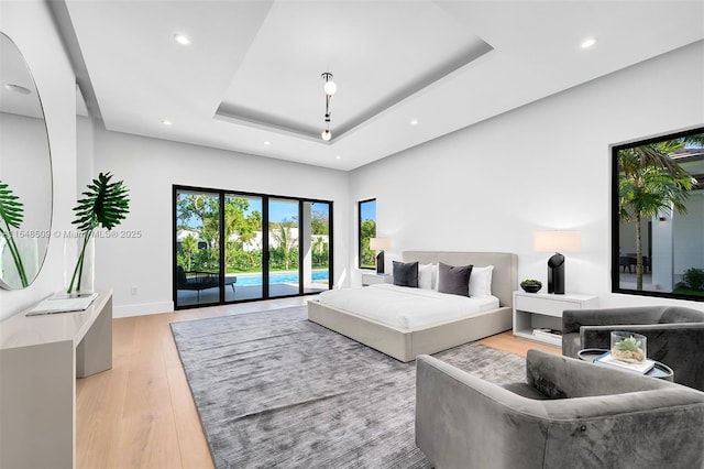 bedroom with a tray ceiling, light hardwood / wood-style floors, and access to outside