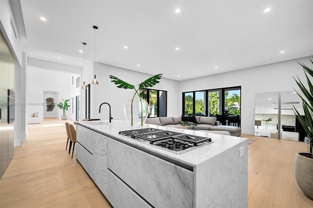 kitchen with stainless steel gas stovetop, a spacious island, hanging light fixtures, light hardwood / wood-style flooring, and light stone countertops