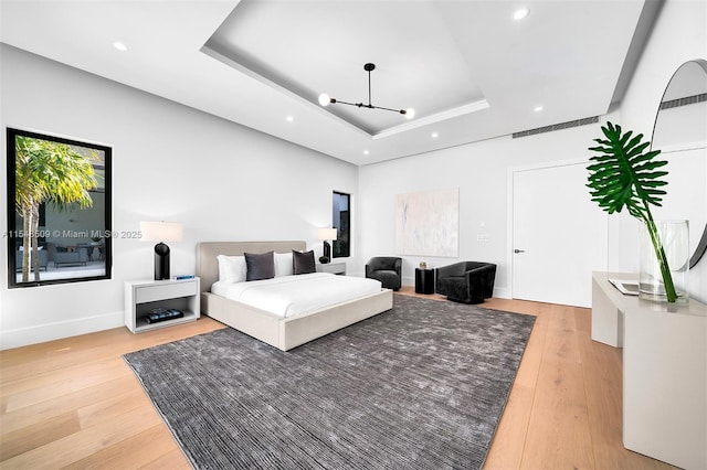 bedroom with a notable chandelier, light hardwood / wood-style floors, and a tray ceiling