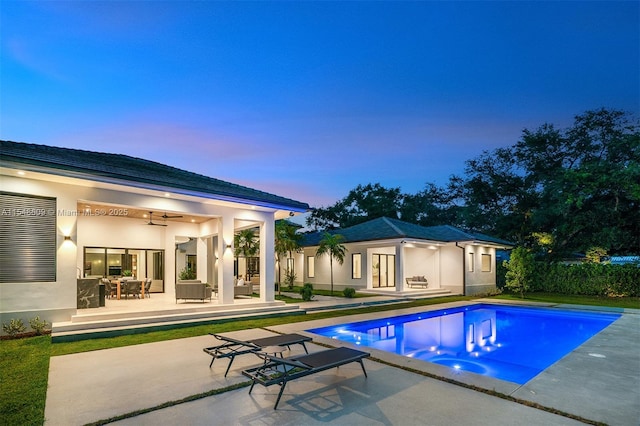 pool at dusk with ceiling fan and a patio area