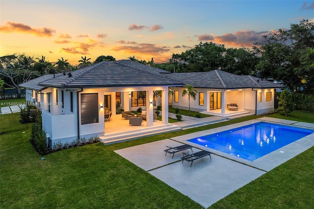 back house at dusk with outdoor lounge area, a yard, and a patio