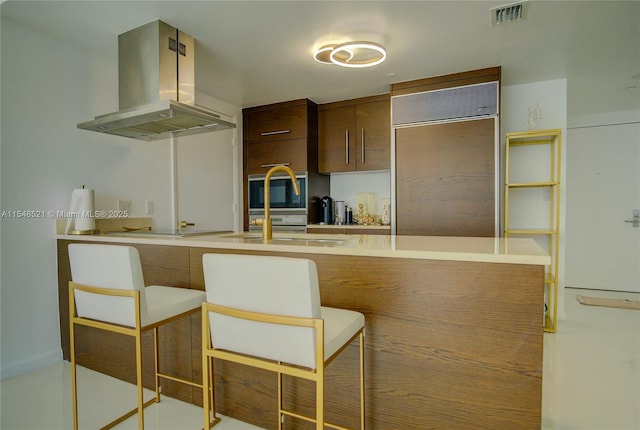 kitchen featuring visible vents, island range hood, a breakfast bar, paneled built in refrigerator, and light countertops