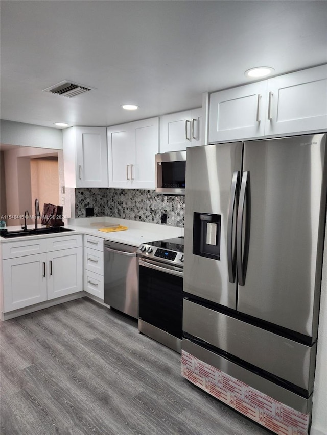 kitchen with white cabinetry, light hardwood / wood-style flooring, stainless steel appliances, backsplash, and sink