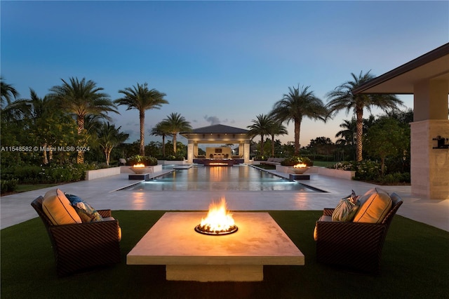 pool at dusk with an outdoor fire pit, area for grilling, a gazebo, and a patio area