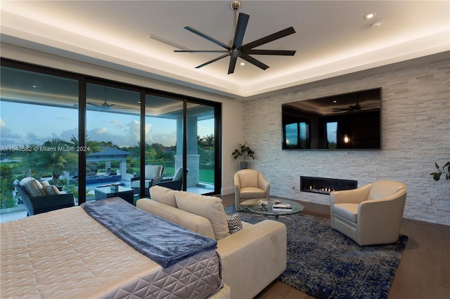 bedroom with hardwood / wood-style floors, ceiling fan, access to exterior, a fireplace, and a raised ceiling