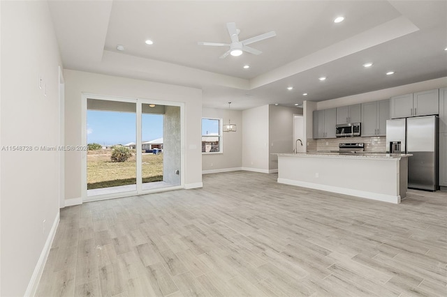 kitchen with backsplash, appliances with stainless steel finishes, a center island with sink, and a tray ceiling