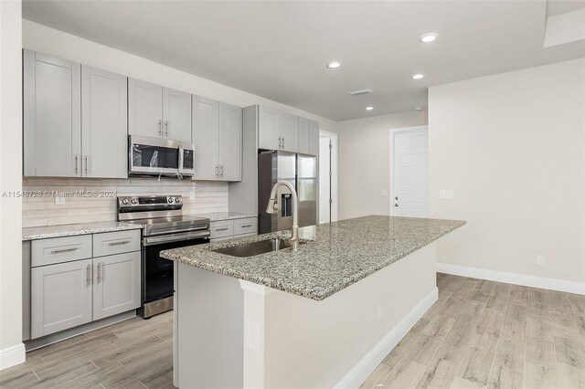 kitchen featuring gray cabinets, stainless steel appliances, sink, and an island with sink