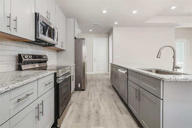 kitchen with light wood-type flooring, backsplash, light stone countertops, appliances with stainless steel finishes, and sink