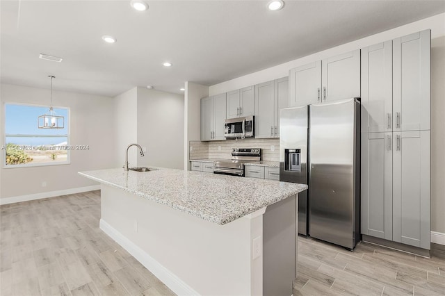 kitchen featuring a center island with sink, appliances with stainless steel finishes, decorative backsplash, and light stone counters