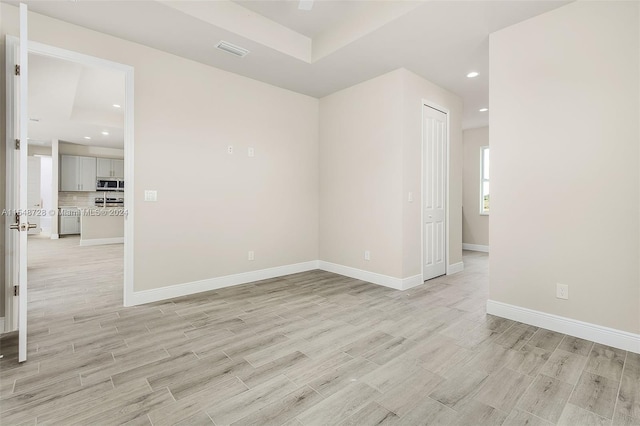 empty room with light hardwood / wood-style floors and a tray ceiling